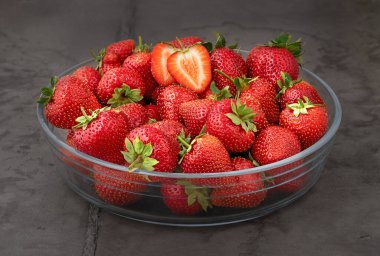 Gri bir arka planda cam bir kasede taze ve lezzetli çilekler.