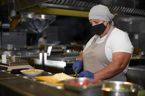 cooking, profession and people concept - woman in age chef wearing protective black mask on her face while working in restaurant kitchen, Corona virus concept