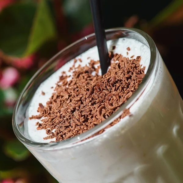 Milkshake with chocolate chips on a summer terrace against the background of flowers. Close up 1:1