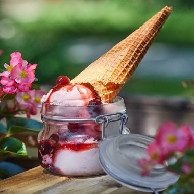 Çiçeklerin arka planında, yaz terasında cam bir kavanozda dondurma..