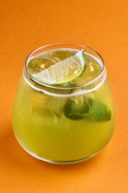 Alkolik fesleğen, yeşil fesleğen, cin, şeker şurubu, limon suyu ve buz ile portakal arkaplanında ezme.