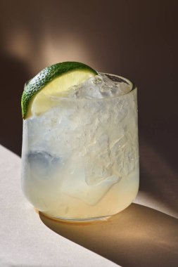 Limon, limon, tonik, turuncu zemin üzerinde votka ve buz, gün ışığı, camı aydınlatan bir güneş ışığı. seçici odak.