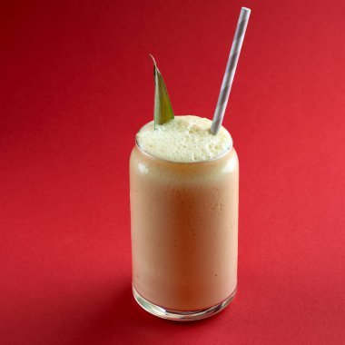 Kırmızı arka planda ananas yaprağıyla süslenmiş bir bardak taze ananas püresi, detoks diyeti kavramı.