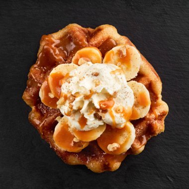 Üzerinde karamel şurubu olan muzlu gözlemeler koyu taştan bir arka planda. Üst Görünüm.