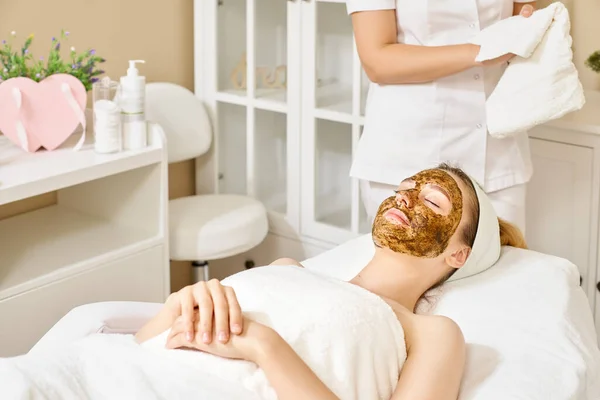 Young woman having face treatment in spa salon, facial scrub for face
