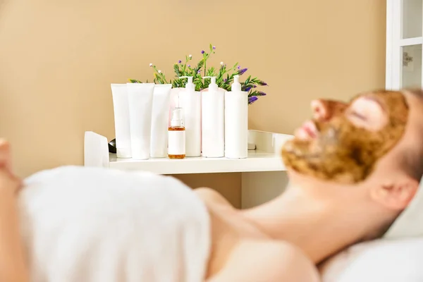 Mockup, tubes and bottles without logos in the spa, face scrub on the girl in the foreground out of focus.