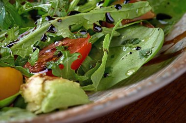 Yeşil yapraklardan, domateslerden ve zeytinyağıyla tatlandırılmış avokadodan yapılmış organik sebze salatası. Kapat.