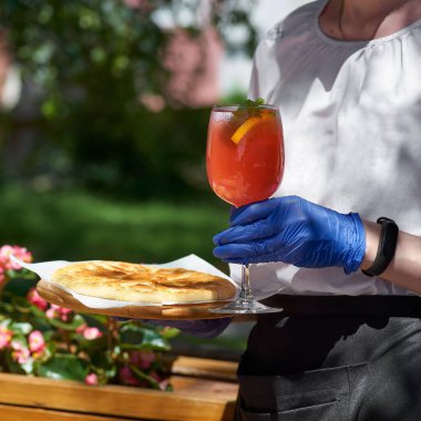 Peynirli vertuta ve bir garsonun elinde bir bardak kırmızı limonata, güneşli bir gün. Restoran konsepti, servis. 1: 1