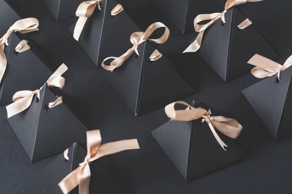 rows of handmade pyramid cardboard boxes with ribbons on black background