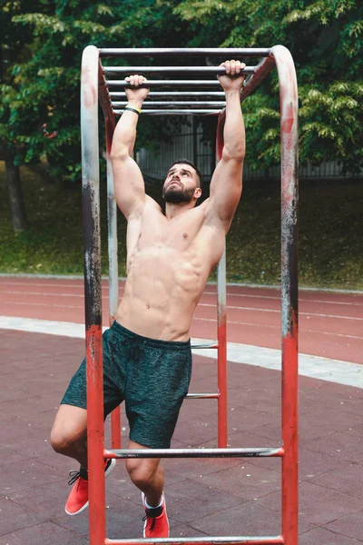 shirtless man doing pull-ups in outdoor scene