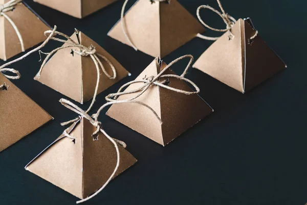 rows of handmade pyramid cardboard boxes with strings on black background