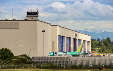 EVERETT, WASHINGTON STATE, USA - JUNE 2018: The massive airplane assembly building at the Boeing factory at Everett. A new, unpainted, jet is in front of the factory. clipart