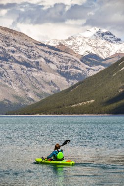 Banff, Ab, Kanada - Haziran 2018: Lake Minnewanka Banff yakınındaki üzerinde küçük bir plastik kayık kürek çekmeye bir ziyaretçi doğal görünümünü.
