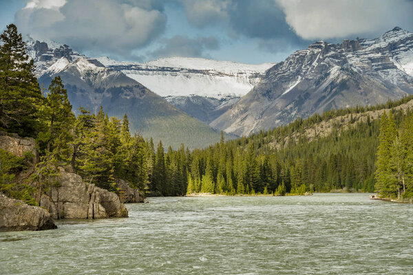 BANFF, AB, CANADA - JUNE 2018: Landscape view of the Bow River, which flows through Banff, with high snow capped mountains in the background.