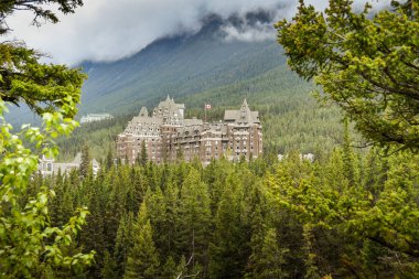 Banff, Ab, Kanada - Haziran 2018: Yaprak dökmeyen ağaçları ile çerçeveli Banff Springs Fairmont Hotel doğal görünümünü.