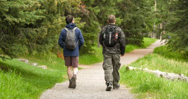 Banff, Ab, Kanada - Haziran 2018: Banff ağaçlık bir alanda bir yol üzerinde yürüyen bir sırt çantası ile sıcak giysiler iki kişi.