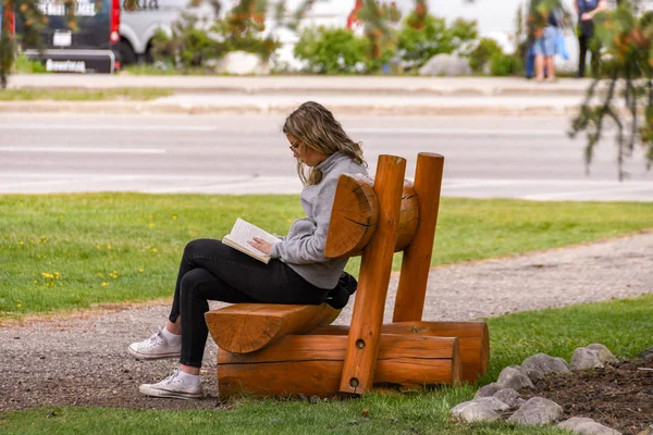 加拿大 的贾斯珀 2018年6月 年轻人坐在艾伯塔省贾斯珀公共公园的木凳上看书 — 图库照片