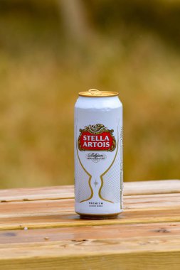 Fairford, İngiltere - Temmuz 2018: Stella olabilir Artois lager bulanık arka planı izole bir açık ahşap piknik masa üzerinde.