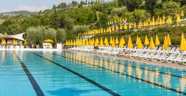 Garda Gölü, İtalya - Eylül 2018: Garda Gölü 'nün dışında, Garda Oteli' nde Olimpiyat büyüklüğünde açık yüzme havuzu, durgun suda güneş şemsiyelerinin yansımaları..