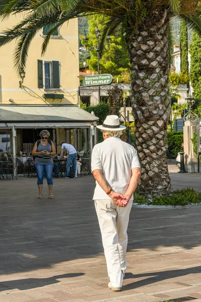 Gardone Riviera, İtalya - Eylül 2018: Kişi güneş şapkası Gardone Riviera kasaba meydanında çevresinde Lake Garda arkasından sıktı elleri ile gezinme.