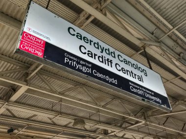 Cardiff, Galler - Ekim 2018: Cardiff Merkez Tren Garı, platform çatıdan askıya iki dilli istasyonu adı işareti. Tabelayı Cardiff Üniversitesi tarafından desteklenmektedir.
