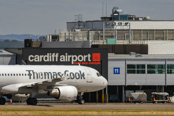 Welcome to Wales sign on the terminal building of Cardiff Wales Airport. A Qatar airways jet is taxiing to the terminal after landing