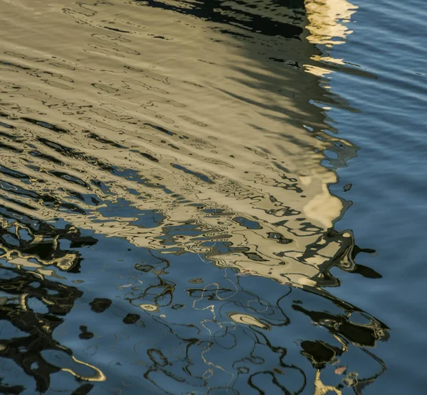 Reflection of the white hull of a boat on rippled water in a marina