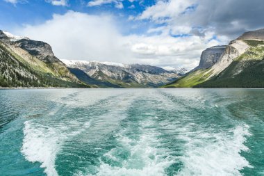 Banff, Ab, Kanada - Haziran 2018: Arka planda göl Minnewanka Banff yakınındaki çevreleyen dağlar kar ile hızlı bir bot izinde şapkalı.