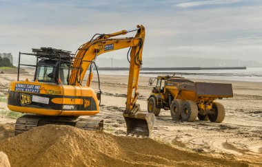 Swansea, Galler - Ekim 2018: Ekskavatör ve rüzgarlar seafront için üflenir sonra Swansea sahilde kum yığınları taşıma kamyonu.