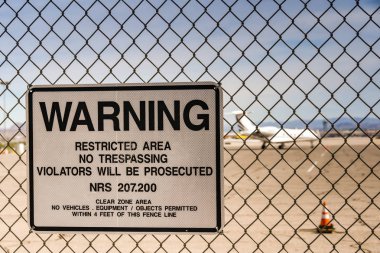 LAS VEGAS, NEVADA, USA - FEBRUARY 2019: Warning sign on a fence around McCarran International Airport. In the background is a private executive jet.