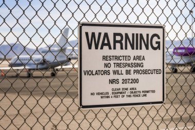 Las Vegas, Nevada, ABD-Şubat 2019: McCarran Uluslararası Havaalanı etrafında bir çit üzerinde uyarı işareti. Arka planda özel yönetici jetleri vardır.