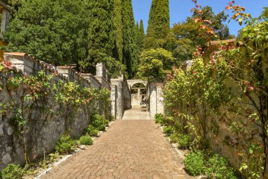 Gardone Riviera, Italya-Eylül 2018: Gardone Rivierası 'ndaki Vittoriale Degli Italian bahçelerinde çiçek bitkileri tırmanma ile iki taş duvarlar arasındaki patika.