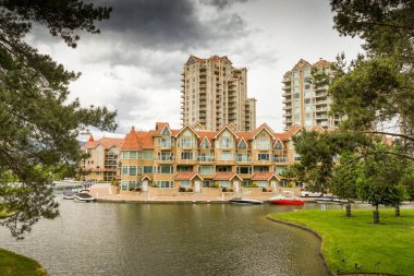KELOWNA, BRITISH COLUMBIA, CANADA - JUNE 2018: The apartments in the Sunset Waterfront resort in Kelowna, British Columbia, Canada, have moorings for boats. clipart