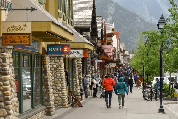 BANFF, AB, CANADA - Haziran 2018: Banff 'ın merkezindeki dükkanların önünden geçen turistler.