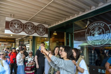 Seattle, Washington State, ABD - Haziran 2018: Seattle şehir merkezindeki Pike Place'deki Starbucks'ın orijinal şubesinin önünde asılı tabela. Bir grup turist selfie çekiyor.