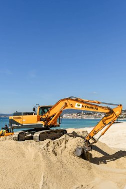 Cannes, Fransa - Nisan 2019: Cannes'daki plajı geliştirmek için kullanılan bir kum yığını üzerinde çalışan ekskavatör, ilkbahar ve yaz tatili sezonuna hazır
