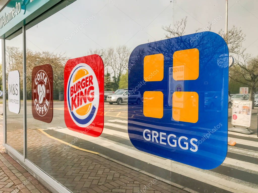 CHIPPENHAM, ENGLAND - APRIL 2019: Logos of food and drink retailers on the mirrored glass window at the entrance to the Leigh Delamere services on the M4 motorway near Chippenham