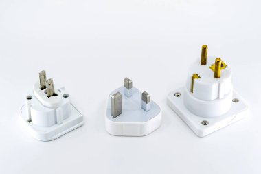 Düz beyaz bir arka plan aleyhine izole şebeke gücü için üç farklı seyahat adaptörü fişinin yakın görünümü. Abd, İngiltere ve Avrupa için adaptörler soldan sağa ar.