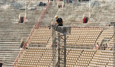 Verona, İtalya - Eylül 2018: Verona Arena'da klasik bir konserden sonra çerçeveyi söken yüksek metal aydınlatma gantry'nin üstünde uzman rigger. Şehir merkezinde bir Roma amfitiyatrosudur..