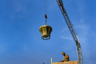 Garda, Garda Gölü, İtalya - Eylül 2018: Garda Gölü'ndeki Garda kasabasındaki bir şantiyede bir işçiye ağır çelik bir beton kovası indiren kule vinç.