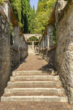 Gardone Riviera, İtalya - Eylül 2018: Gardone Riviera'daki Vittoriale degli Italiani bahçelerinde iki taş duvar arasındaki basamaklı patika.