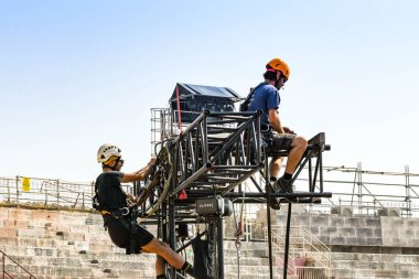Verona, İtalya - Eylül 2018: Verona Arena'da yapılan klasik konserin ardından çerçeveyi söken uzun bir metal aydınlatma gantry'nin üstünde uzman riggers. Şehir merkezinde bir Roma amfitiyatrosudur..