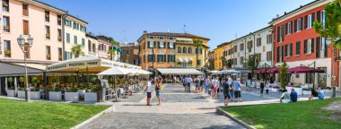 Sirmione, Garda Gölü, İtalya - Eylül 2018: Garda Gölü'ndeki Sirmione limanının yakınındaki meydanda insanların panoramik görünümü. Meydanın çevresinde restoranlar ve oteller vardır.