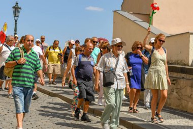 Prague Castle yakınındaki bir sokakta bir tur rehberi takip turist Prag, Çek Cumhuriyeti - Temmuz 2018: grup. Tur rehberi olarak bir bayrak kadar parlak renkli çiçek tutuyor.