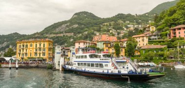 VARENNA, LAKE COMO, ITALY - JUNE 2019: Panormaic view of a passenger and car ferry unloading at the jetty in Varenna on Lake Como. clipart
