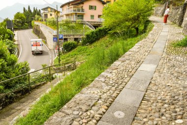 Como Gölü, İtalya - Haziran 2019: Come Gölü'nün bir kısmı boyunca uzanan bir yürüyüş parkurunda metal marker ile yürüyüş yolu - Greenway del Lago di Como. Solda gölün etrafındaki ana yol var..
