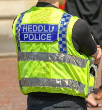 Cardiff, Galler-Temmuz 2019: Cardiff 'te bir polis memurunun yeleğine yakın. Arkadaki tabela iki dilli.