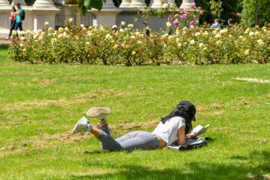Cardiff, Galler - Temmuz 2019: Cardiff'te halka açık bir parkta çimlerin üzerinde yatan öğrenci kitap okuyor .