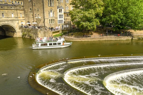 Bath, İngiltere - Temmuz 2019: Bath'ın merkezinde Avon Nehri üzerinde pulteney Weir şeklinde at nalı şeklinde. Bir turist teknesi arka planda.