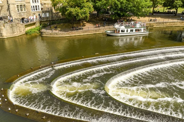 Bath, İngiltere - Temmuz 2019: Bath'ın merkezinde Avon Nehri üzerinde pulteney Weir şeklinde at nalı şeklinde. Bir turist teknesi arka planda.